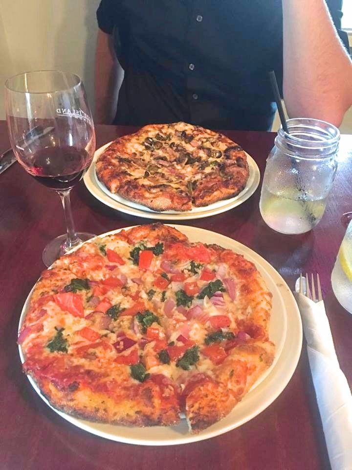 two small pizzas on a table with a glasss of wine and a couple glasses of water