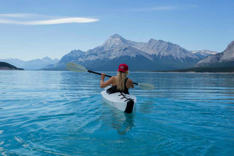 woman kayaking in a large body of water with mountains in the background