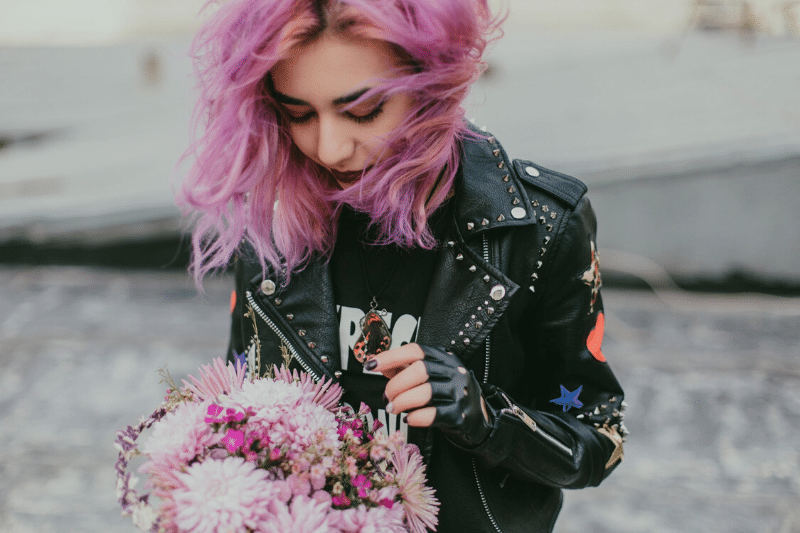 close up of a woman with pink hair wearing a leather jacket and holding a bouquet of pink flowers
