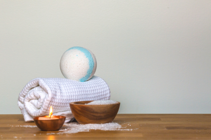 blue and white bathbomb sitting on a towel on a wooden surface next to a lit candle and a bowl of bath salts