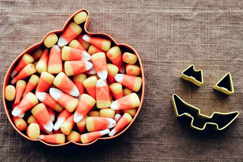 pumpkin shaped bowl full of candy corn next to cookie cutters in the shape of the face of a jack-o-lantern