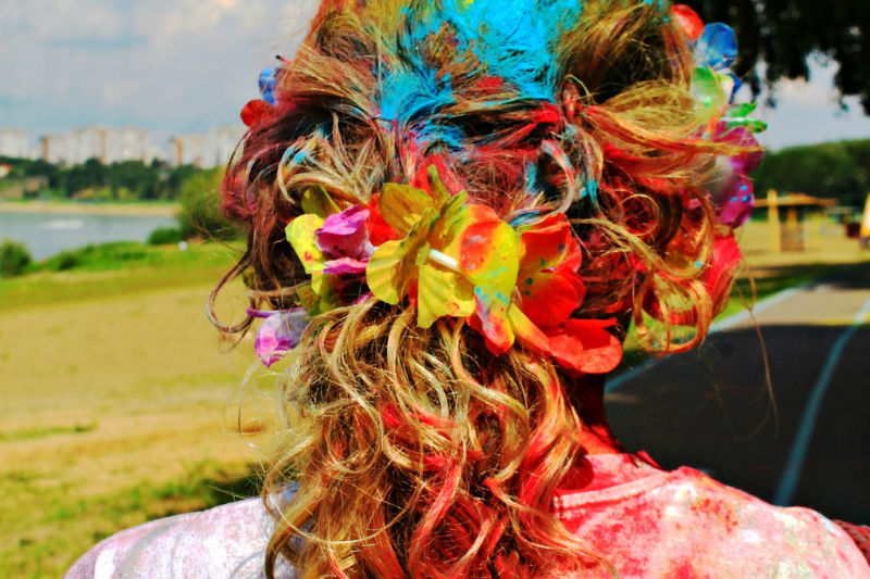 The back of a woman's head, her hair tied back and full of colour, with colour all over her white shirt