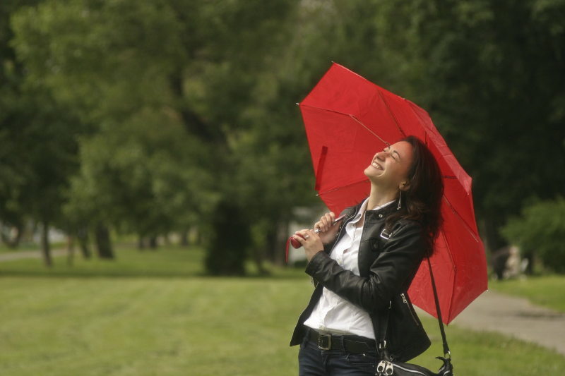 woman standing outside in a park area, looking up at the sky while holding a red umbrella