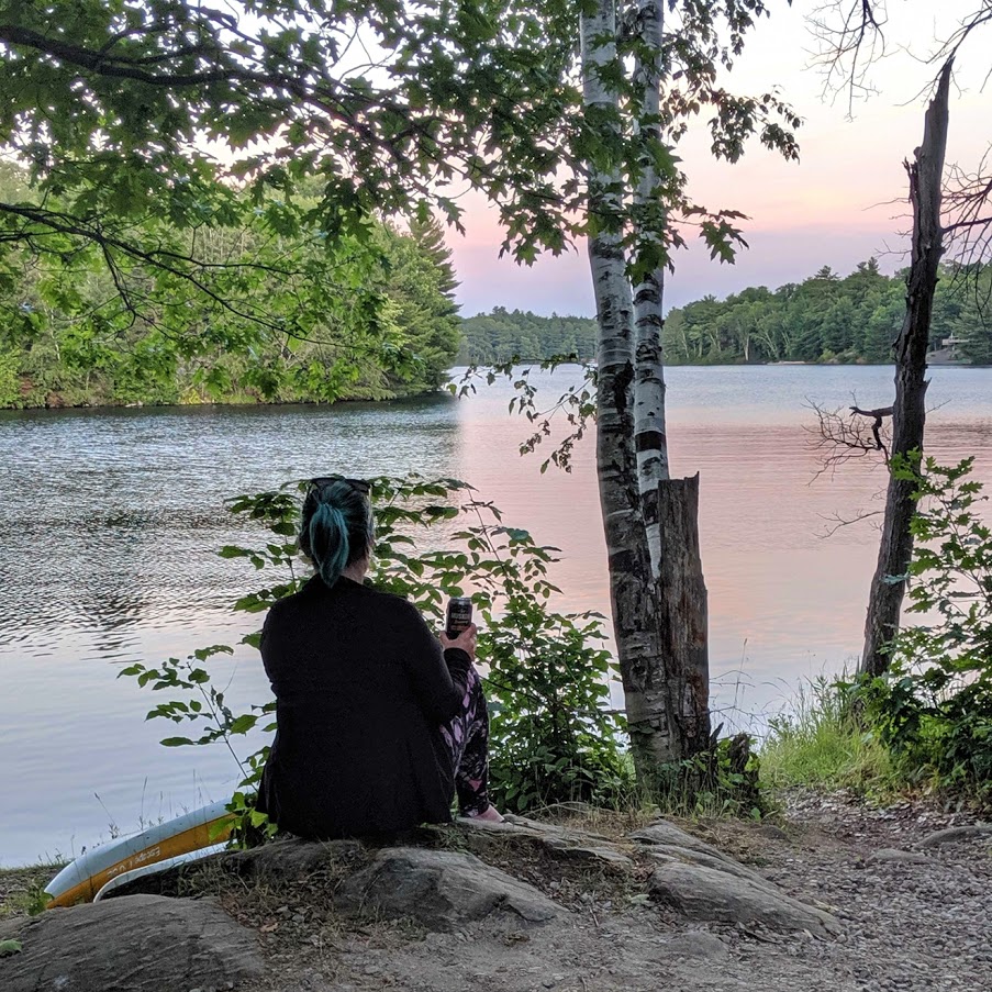 woman sitting on the shores of a lake during sunset