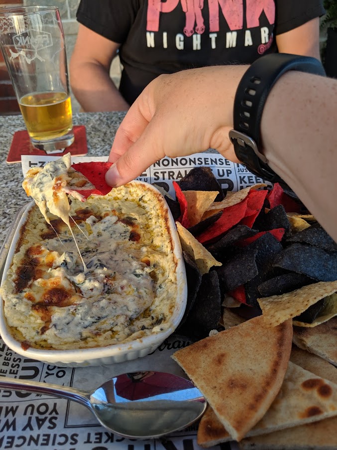 hand dipping a tortilla chip into spinach dip