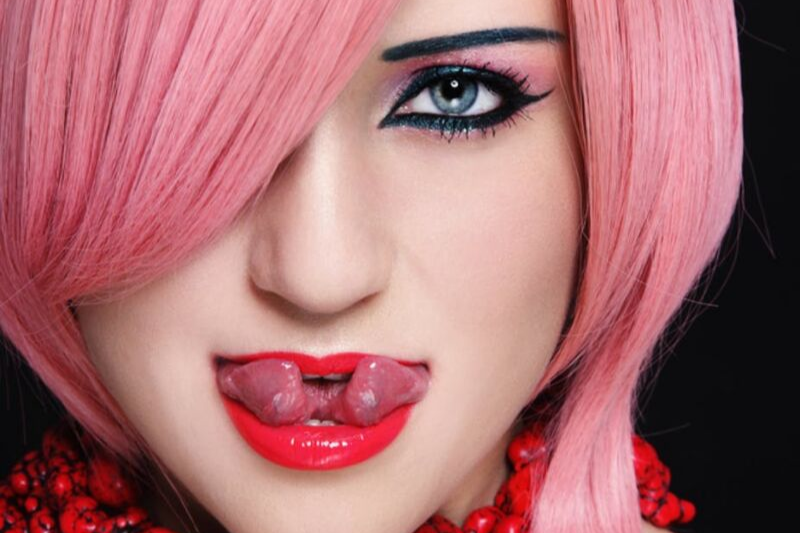 close-up of a woman with pink hair, bold black cat eye style eyeliner and a split tongue