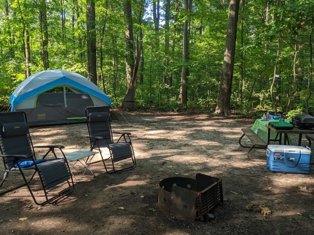 campsite with a tent, chairs, campfire pit and picnic table in the woods