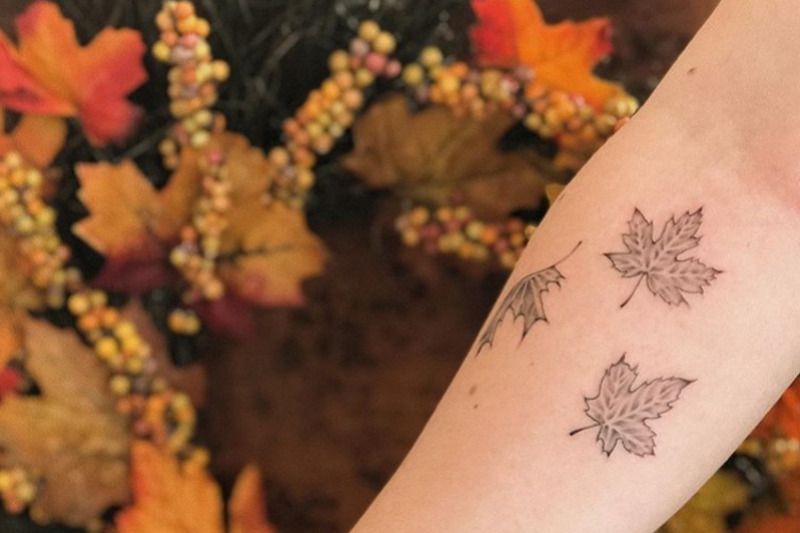 tattoo of leaves on a person's arm held out in front of a background of autumn leaves
