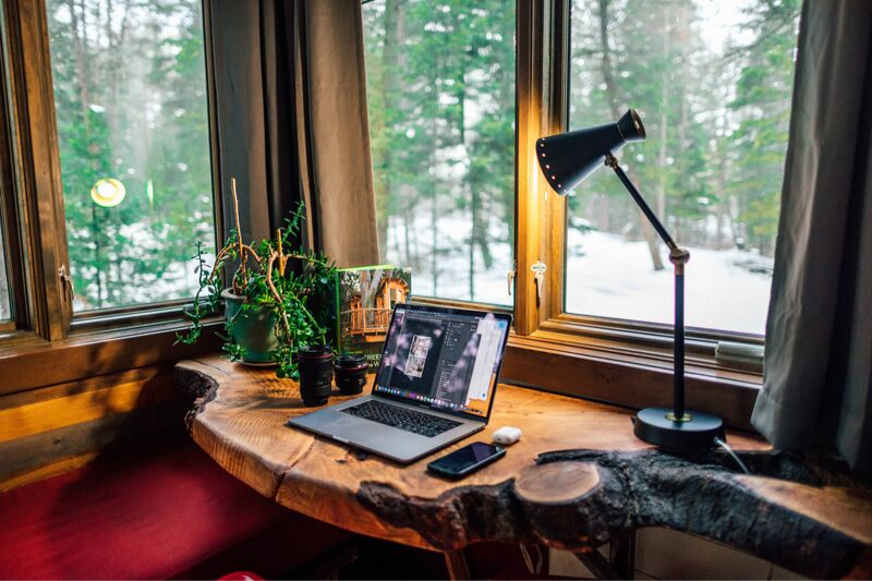 laptop sitting on a natural wood desk in front of a window revealing a snowy forest view