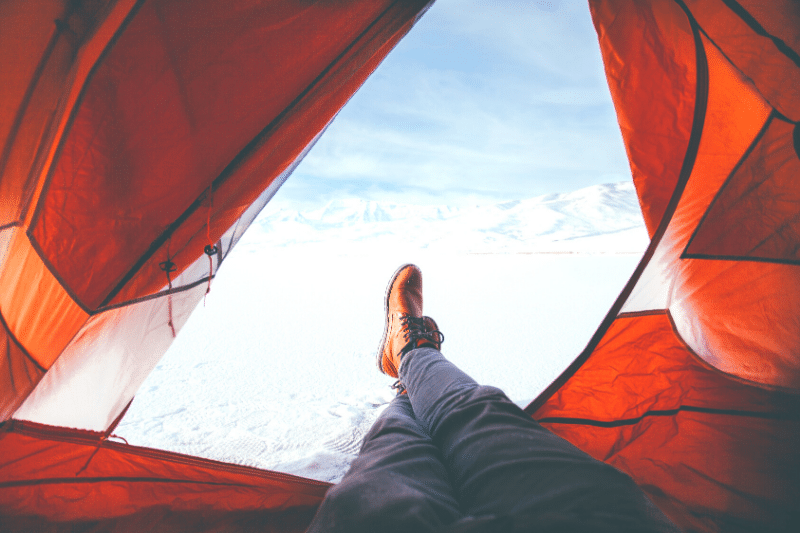 a person's feet sticking out the door of an orange tent, looking out onto the snow