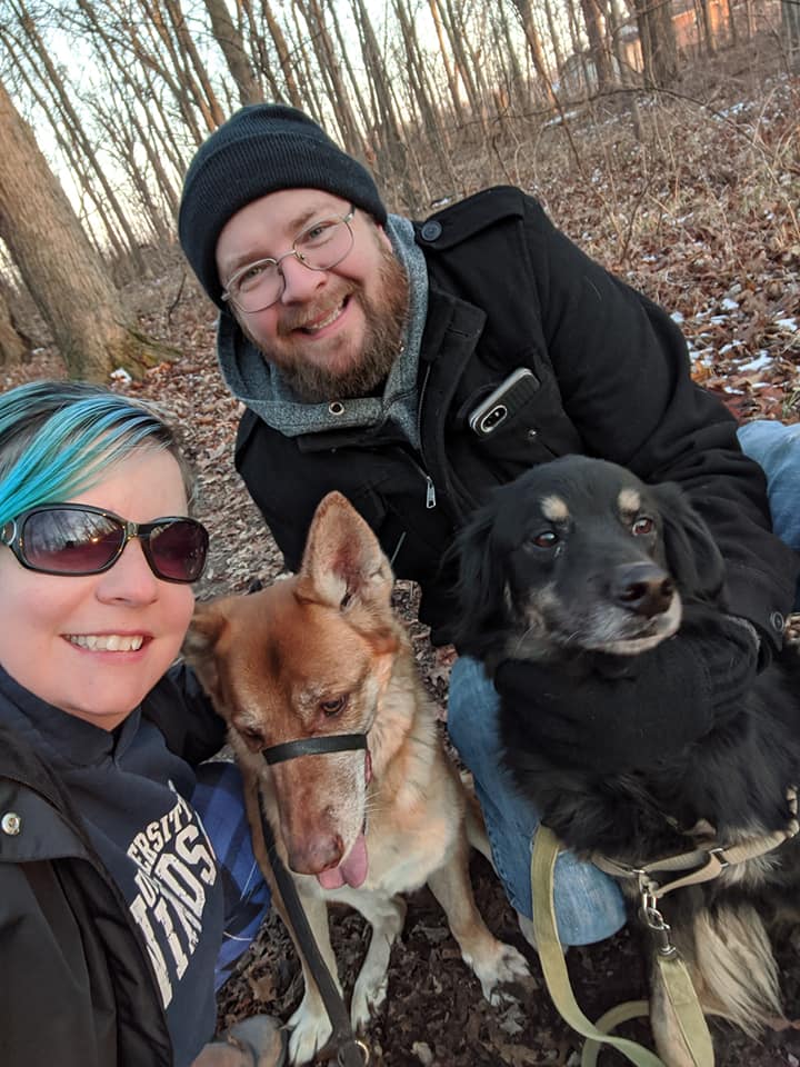 selfie of a young couple with their large dogs while on a hike in a forested area