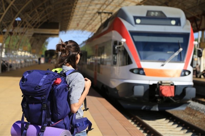 woman with brunette hair and a blue backpack waiting for a train