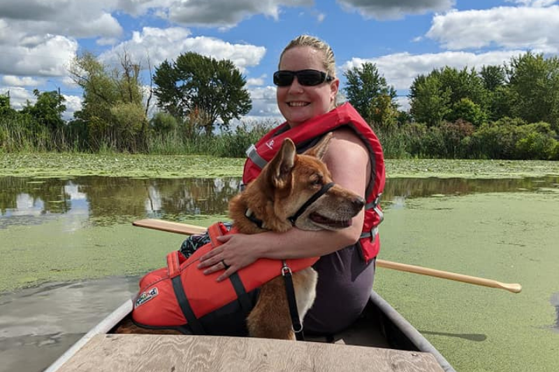 Woman sitting in a canoe wearing a red life jacket and sunglasses, a German Shepherd dog next to her