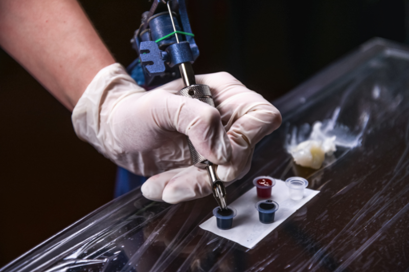tattoo artist dipping tattoo gun in ink | Things to Consider Before Getting a Tattoo