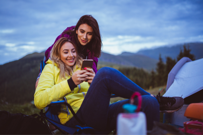 two women looking at smartphone at campsite | Five Reasons Why Your Smartphone is an Important Tool When Camping