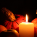 white candle burning in the dark with pumpkins and apples sitting around it