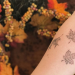 tattoo of leaves on a person's arm held out in front of a background of autumn leaves